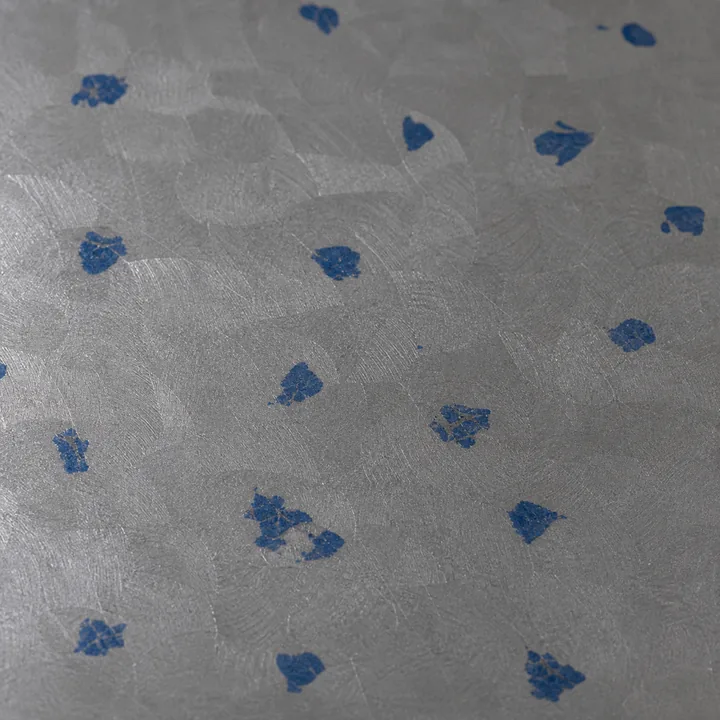 Close-up of a hand-scraped cast-iron surface early in the work: about eighteen large patches of blue marking compound sitting on the high spots, with bare grey iron between them.